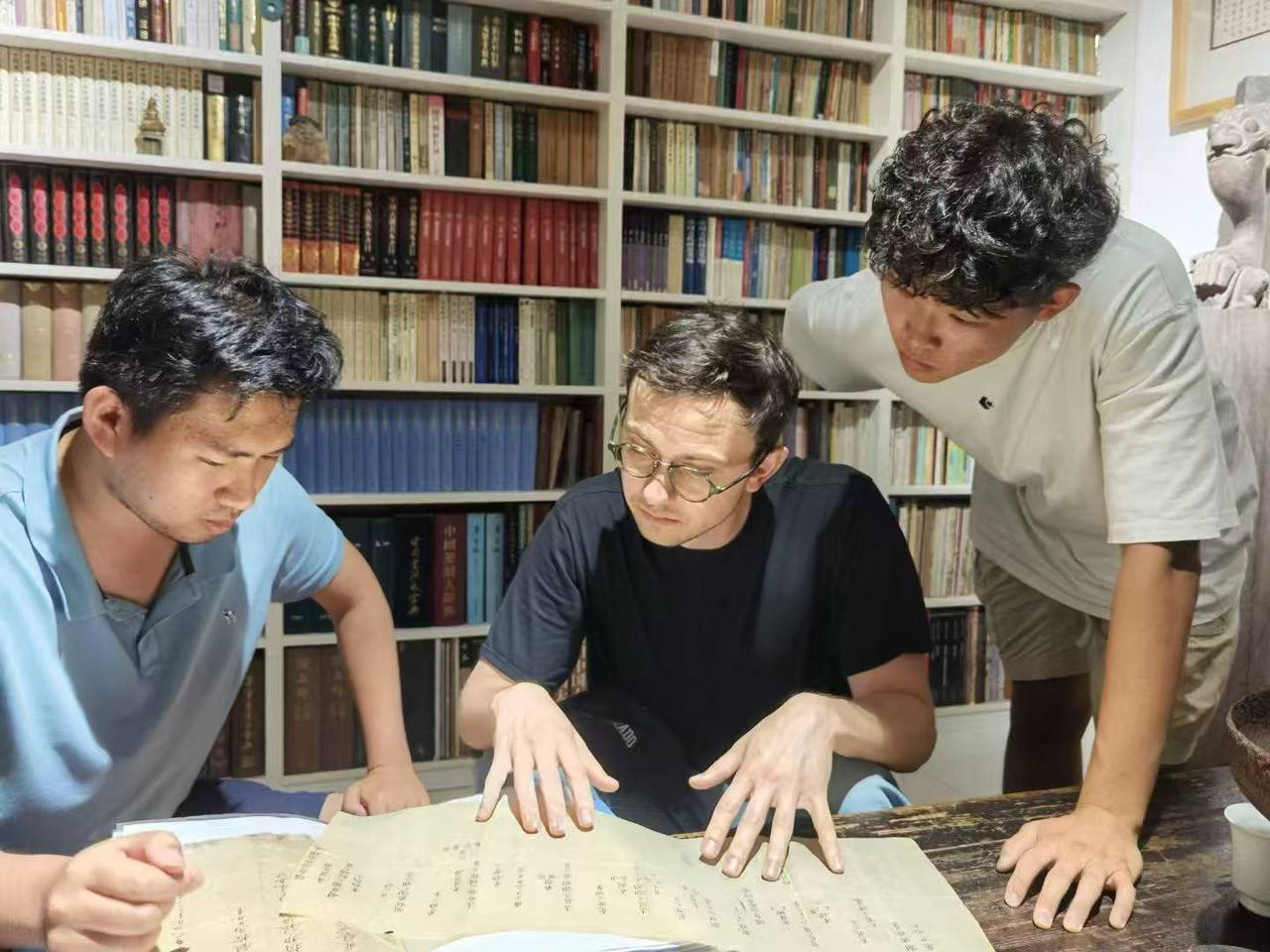 Charles Argon and two students reading a Qing manuscript register at a table,
              in a room lined with shelves of Chinese books.